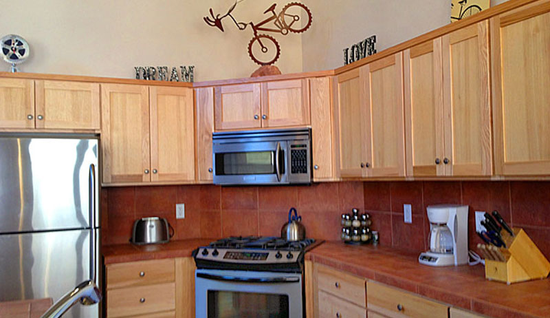 Natural wood color cupboards, stainless steel refrigerator, gas stove and microwave are included in the kitchen in the Unit #19 townhouse at Moab Springs Ranch.